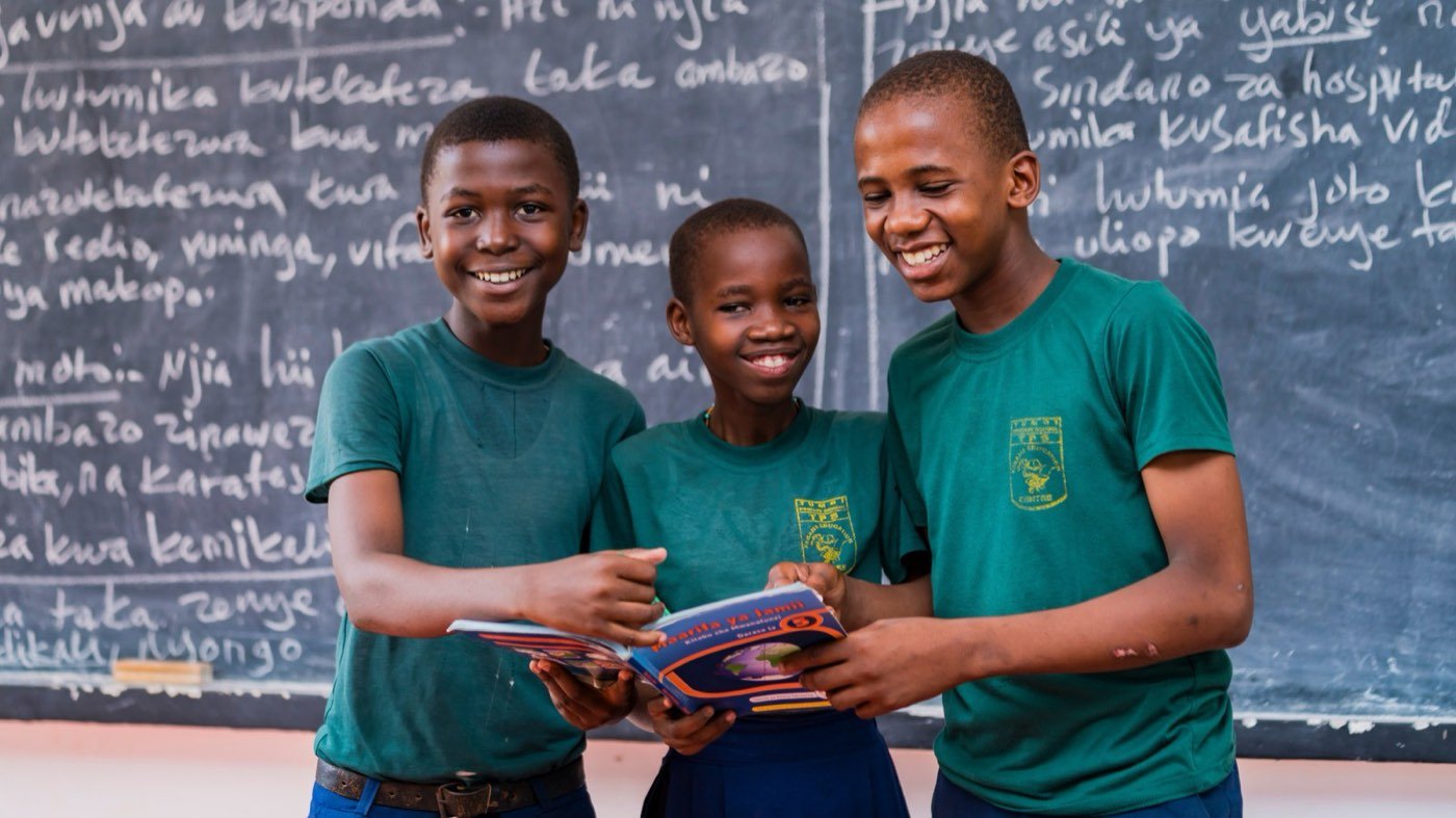 Three pupils reading together in front of a chalkboard